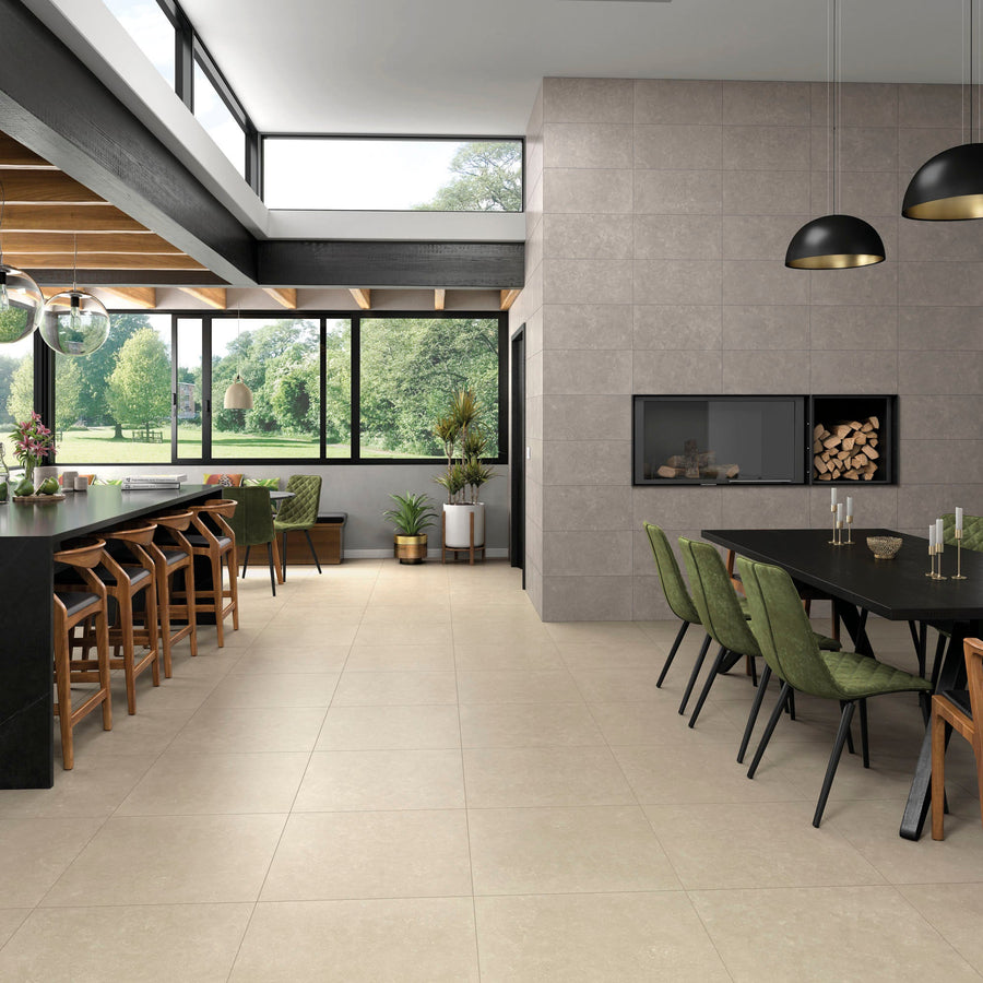 Modern dining area with large windows, wooden ceiling beams, neutral tile flooring, and tiled wall housing a fireplace. Black tables paired with green and brown chairs. Lush garden view.