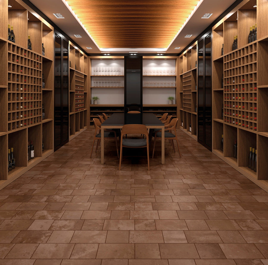 Modern wine cellar with wooden shelving, glassware, and a long table surrounded by chairs, featuring warm lighting and a marbled brown and beige tiled floor.
