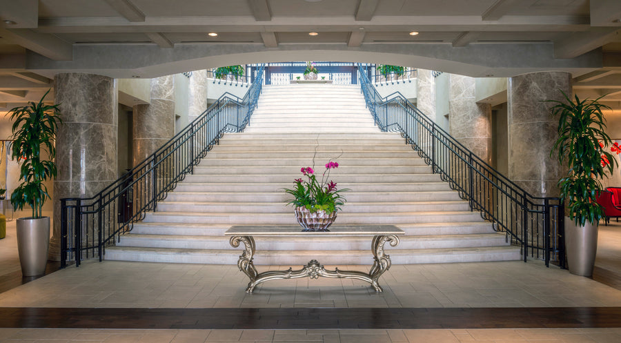 Elegant hotel lobby featuring a grand stone staircase, potted plants, and a decorative table with flowers at the center.
