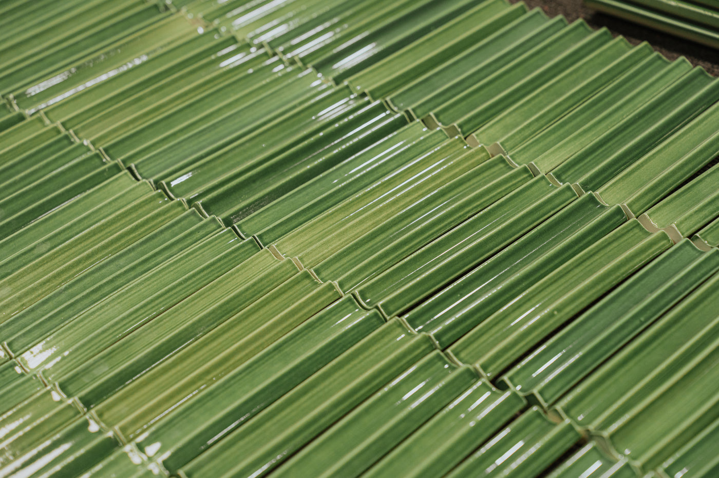Close-up of glossy, green rectangular tiles laid in an overlapping pattern, varying in shades, resembling bamboo.